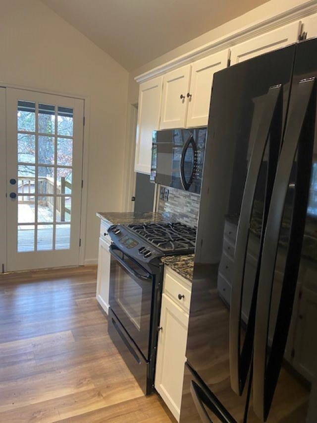 kitchen featuring white cabinets, vaulted ceiling, light wood-type flooring, black appliances, and dark stone countertops