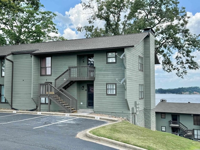 view of front facade with a chimney, uncovered parking, a shingled roof, a water view, and stairway