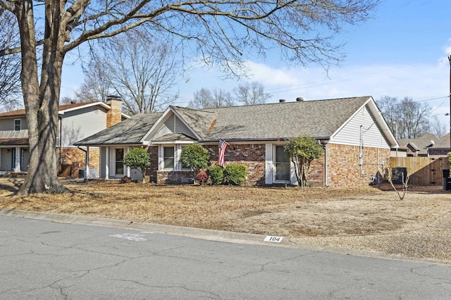 view of front of house featuring a shingled roof, brick siding, fence, and a chimney