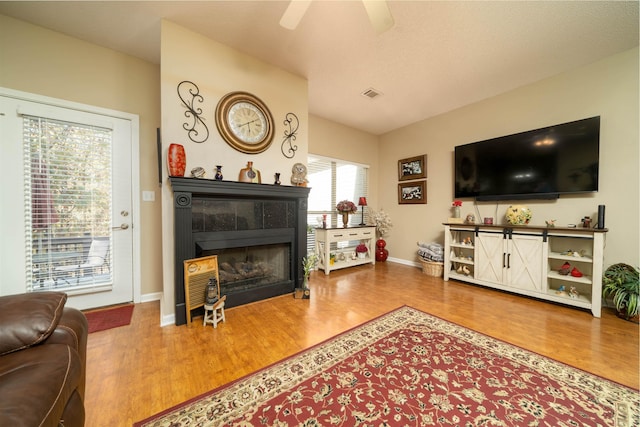 living area featuring lofted ceiling, visible vents, a fireplace, and wood finished floors