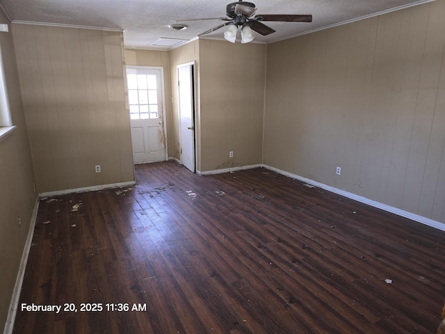 empty room featuring a textured ceiling, a ceiling fan, baseboards, ornamental molding, and dark wood finished floors