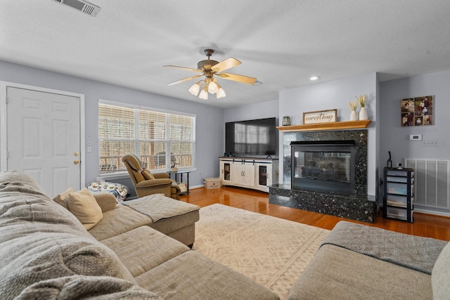 living room featuring light wood-style floors, ceiling fan, a fireplace, and visible vents