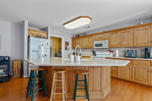 kitchen featuring white appliances, a center island with sink, visible vents, light wood-style flooring, and light stone counters