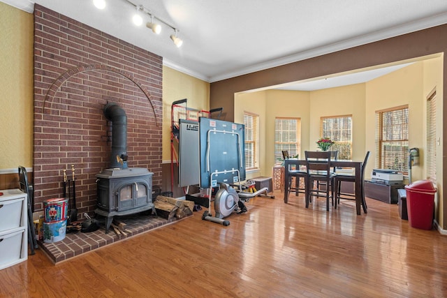 living room featuring a wood stove, rail lighting, crown molding, and wood finished floors