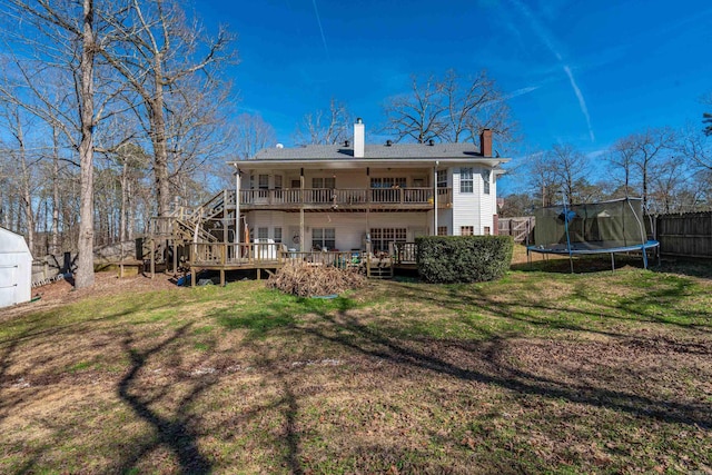 rear view of property with a deck, fence, a lawn, a trampoline, and a chimney