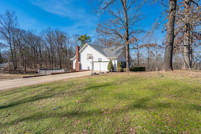 exterior space with driveway, a chimney, and a lawn