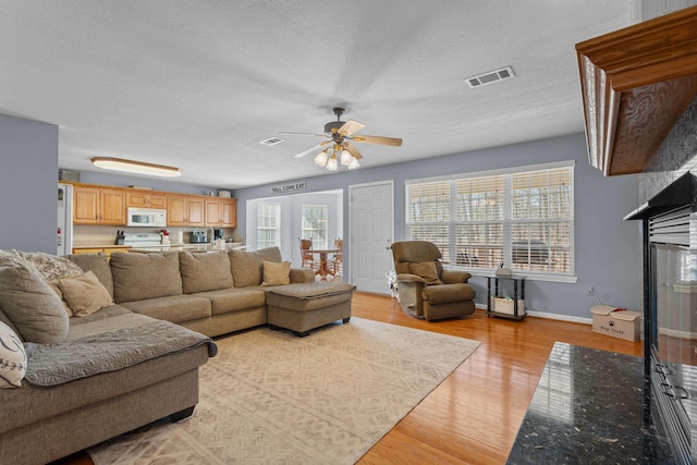 living area featuring light wood-style floors, baseboards, visible vents, and a textured ceiling