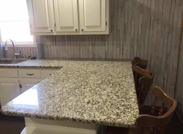 kitchen with white cabinetry, a sink, wood walls, and light stone countertops