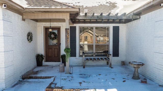 snow covered property entrance with a shingled roof and brick siding