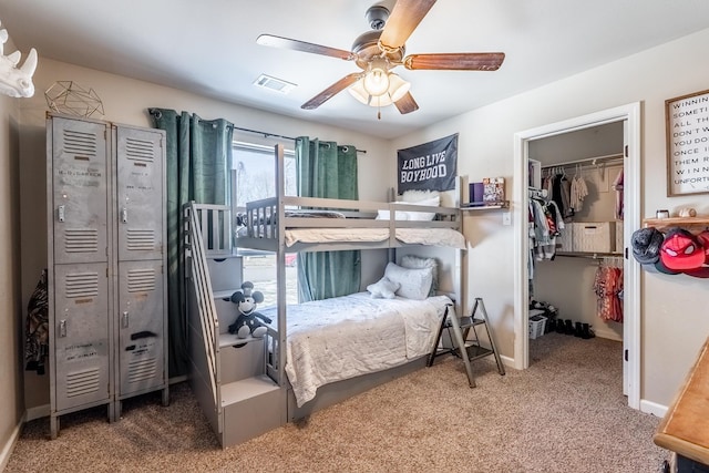 carpeted bedroom with baseboards, visible vents, ceiling fan, a walk in closet, and a closet