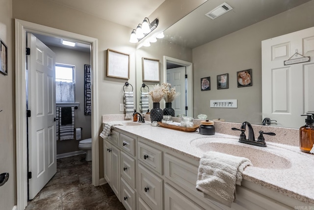 full bath with toilet, double vanity, a sink, and visible vents