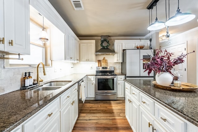 kitchen featuring pendant lighting, appliances with stainless steel finishes, white cabinets, a sink, and wall chimney range hood