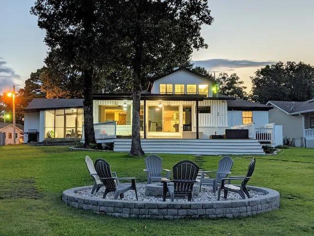 back of house at dusk featuring a deck, a patio, an outdoor fire pit, and a lawn