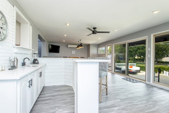 kitchen featuring a breakfast bar, light countertops, white cabinets, a sink, and a peninsula