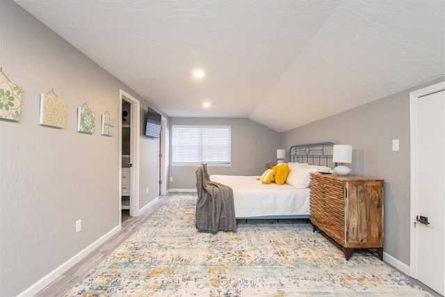 bedroom featuring lofted ceiling, a textured ceiling, wood finished floors, and baseboards