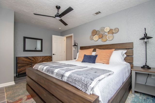 bedroom featuring visible vents, a ceiling fan, a textured ceiling, wood finished floors, and baseboards