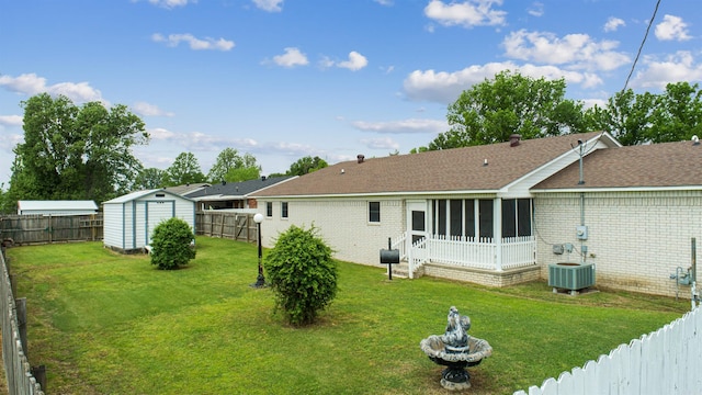 back of property featuring a lawn, a fenced backyard, an outbuilding, a sunroom, and a storage unit