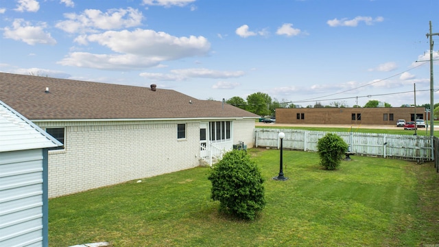 rear view of house featuring fence, brick siding, entry steps, a shingled roof, and a yard