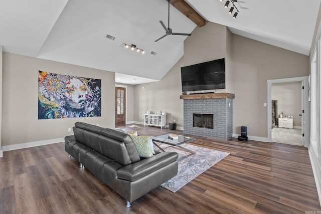 living area with baseboards, a ceiling fan, dark wood-style flooring, beamed ceiling, and a brick fireplace