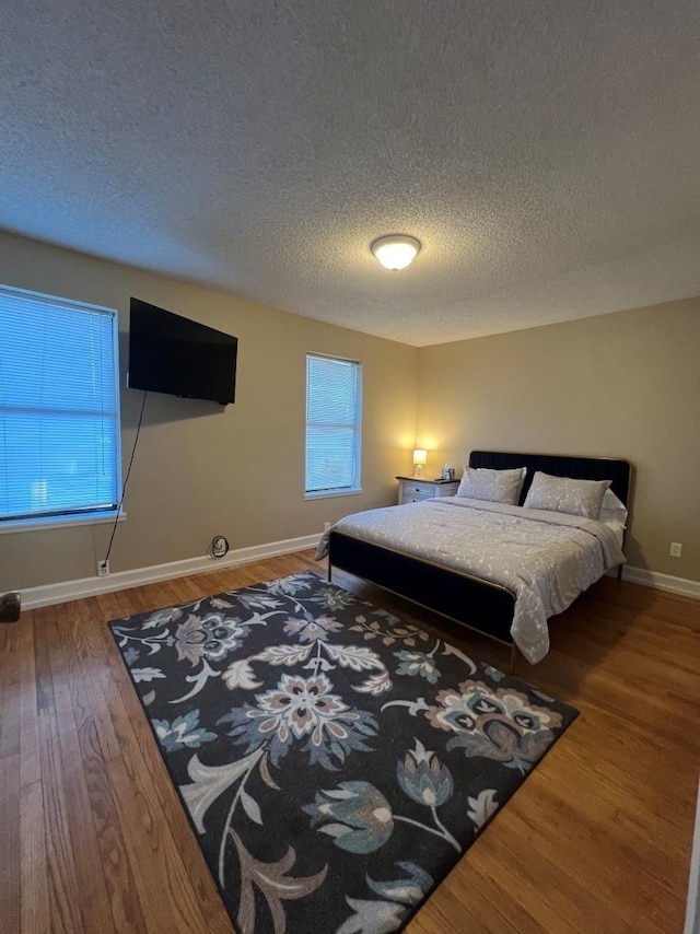 bedroom with a textured ceiling, wood finished floors, and baseboards