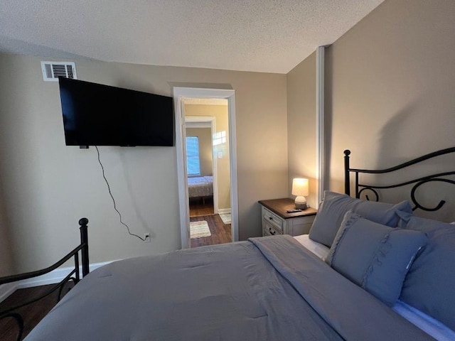 bedroom featuring baseboards, a textured ceiling, visible vents, and wood finished floors