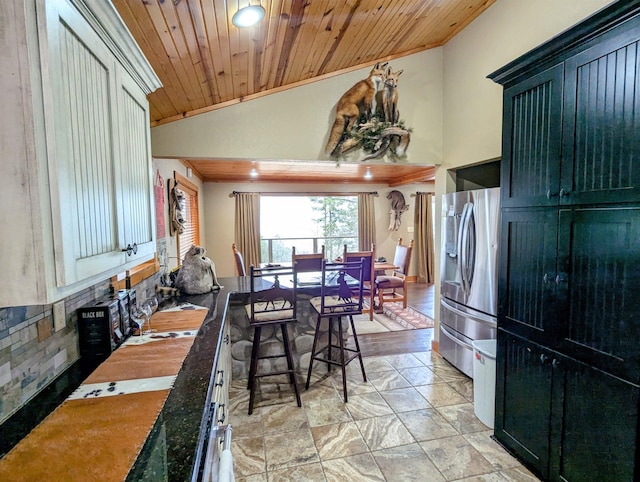 kitchen with vaulted ceiling, wooden ceiling, dark stone countertops, and stainless steel fridge with ice dispenser