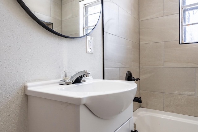 full bathroom featuring a textured wall, a bathtub, and vanity