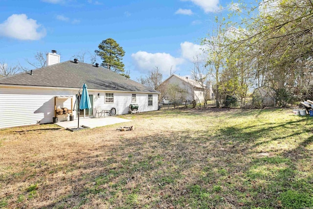 back of house with a fenced backyard, a yard, roof with shingles, a chimney, and a patio area