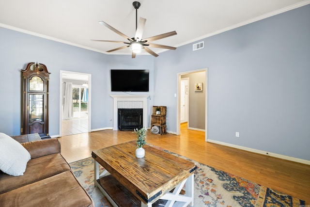 living room featuring a fireplace, visible vents, light wood-style flooring, ornamental molding, and a ceiling fan