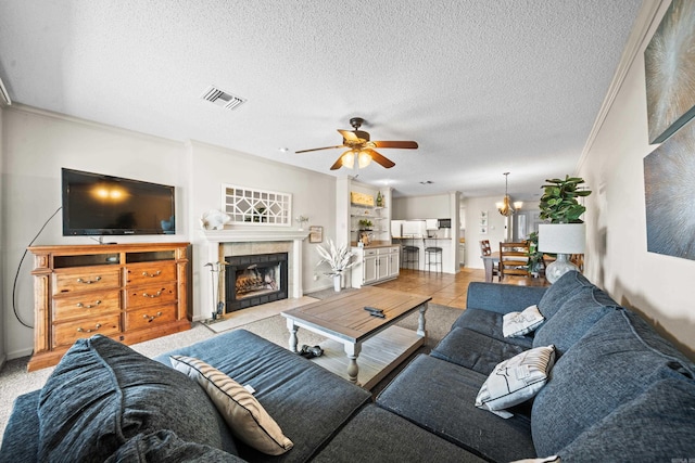 living area featuring a textured ceiling, ceiling fan with notable chandelier, a fireplace, visible vents, and ornamental molding