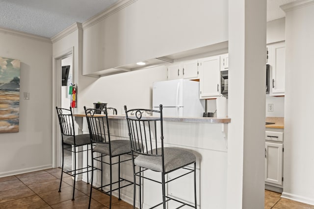 kitchen with a textured ceiling, white cabinetry, a kitchen breakfast bar, light countertops, and freestanding refrigerator