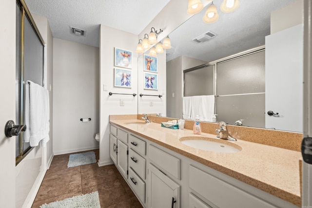 full bath featuring a shower with door, a textured ceiling, visible vents, and a sink