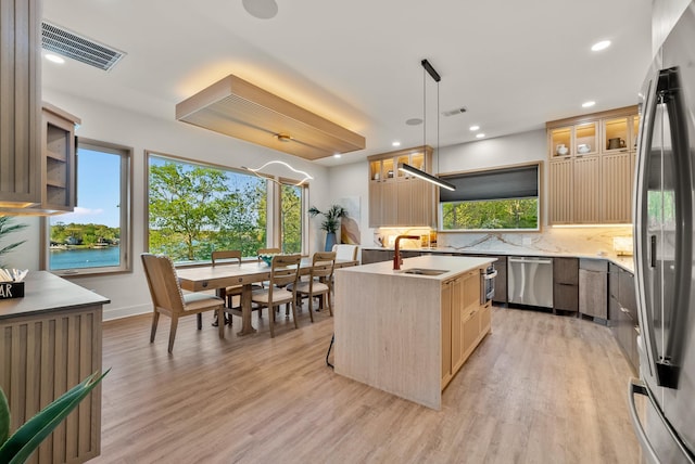 kitchen with visible vents, glass insert cabinets, hanging light fixtures, a kitchen island with sink, and light countertops