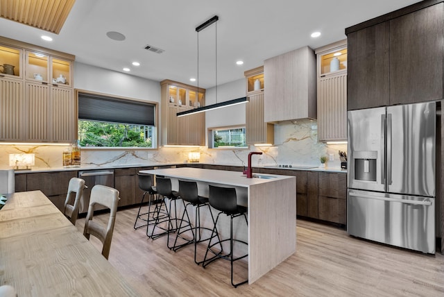 kitchen with an island with sink, appliances with stainless steel finishes, light countertops, and glass insert cabinets