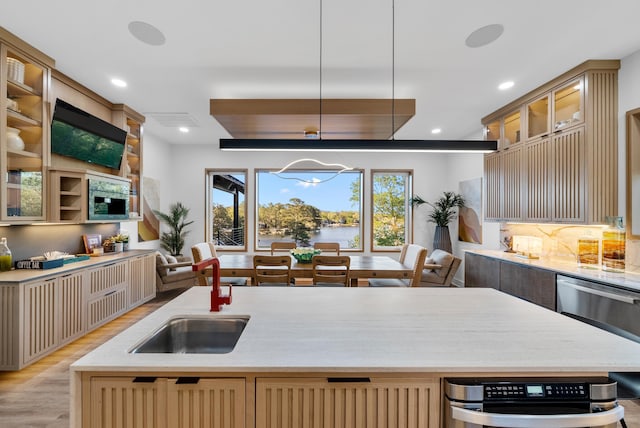 kitchen with a center island with sink, glass insert cabinets, light wood-style floors, pendant lighting, and a sink