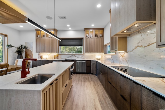 kitchen featuring custom range hood, glass insert cabinets, decorative light fixtures, black electric stovetop, and a sink