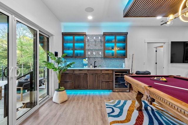 bar featuring beverage cooler, backsplash, indoor wet bar, light wood-type flooring, and a sink