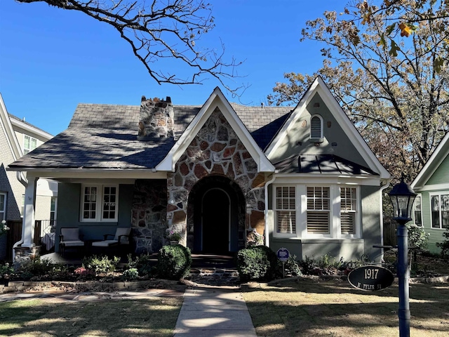 tudor home with stone siding, a chimney, and covered porch