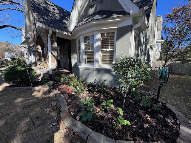 view of property exterior featuring a shingled roof, fence, and stucco siding