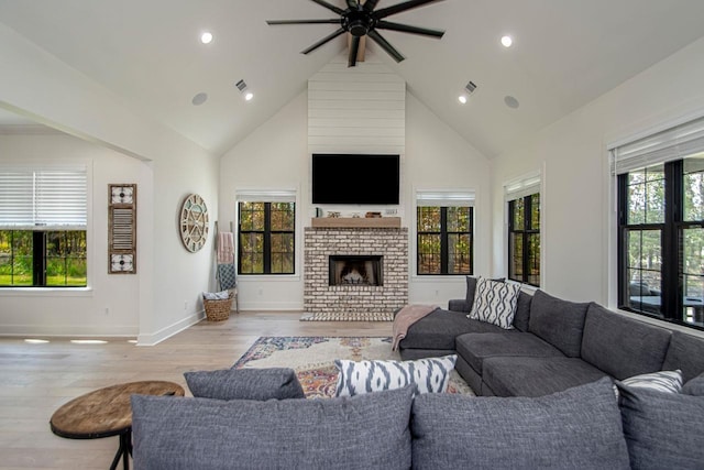 living room with high vaulted ceiling, a brick fireplace, light wood-style flooring, and a healthy amount of sunlight