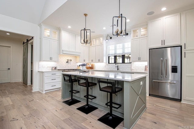 kitchen with a barn door, a kitchen island, glass insert cabinets, stainless steel appliances, and light countertops