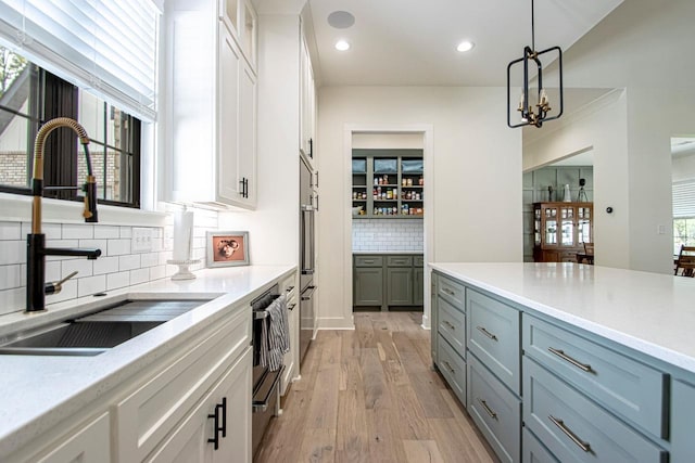 kitchen featuring light wood-style flooring, glass insert cabinets, white cabinetry, pendant lighting, and a sink