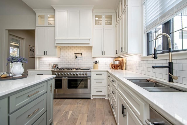 kitchen with appliances with stainless steel finishes, white cabinetry, glass insert cabinets, and a sink