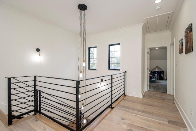 hall with light wood-type flooring, attic access, crown molding, and an upstairs landing