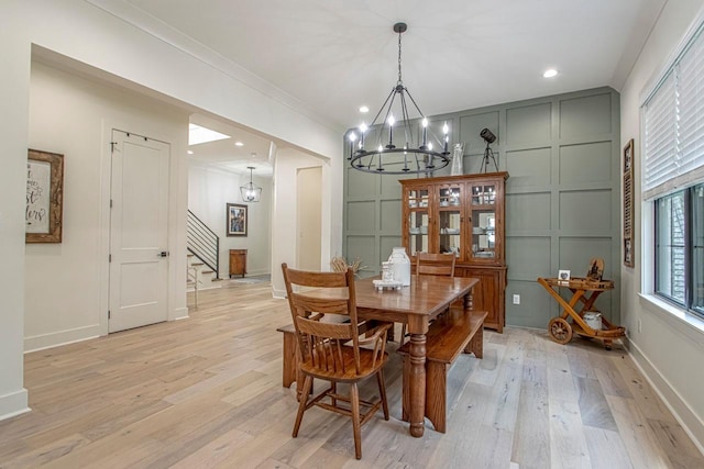 dining space featuring crown molding, a notable chandelier, light wood finished floors, a decorative wall, and stairs