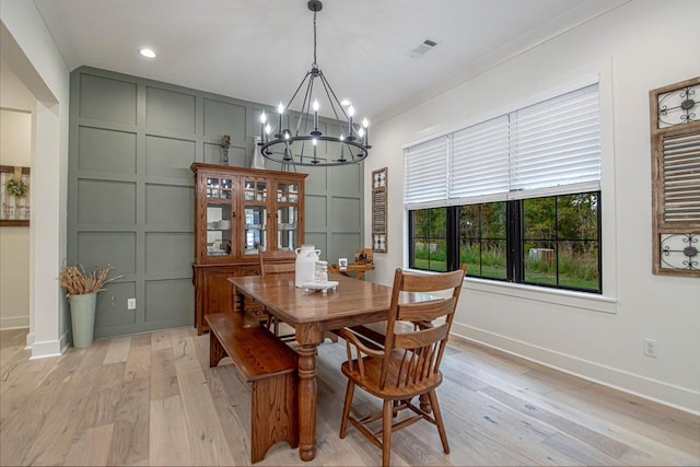 dining room featuring baseboards, ornamental molding, light wood-style floors, a chandelier, and a decorative wall