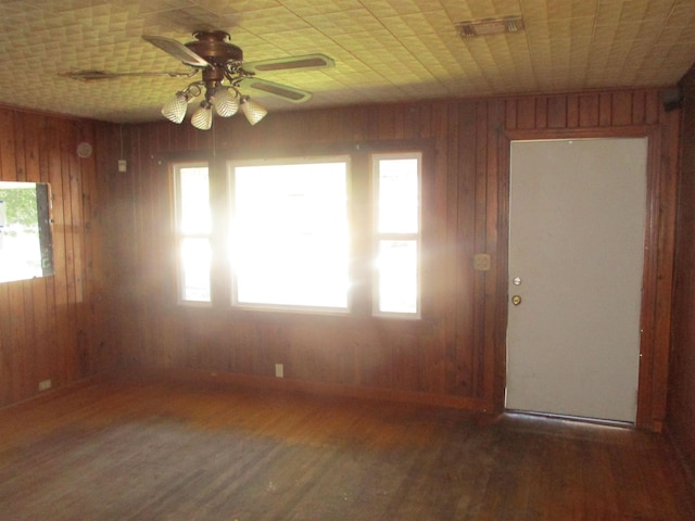 empty room featuring baseboards, dark wood finished floors, a ceiling fan, and wooden walls