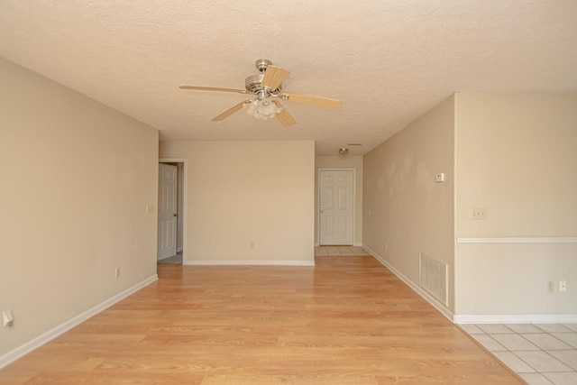 empty room featuring a textured ceiling, ceiling fan, visible vents, baseboards, and light wood-style floors