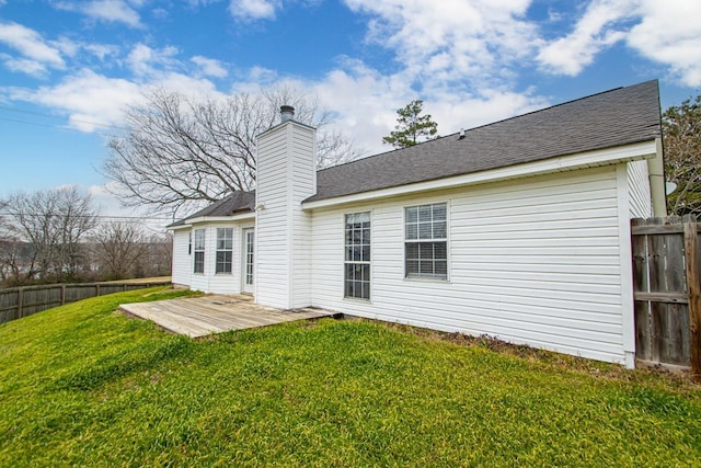 rear view of house with fence, roof with shingles, a lawn, a wooden deck, and a chimney