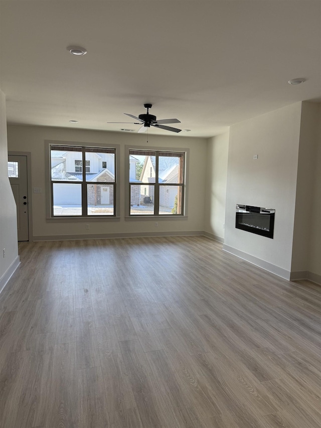 unfurnished living room featuring light wood-type flooring, a glass covered fireplace, a ceiling fan, and baseboards